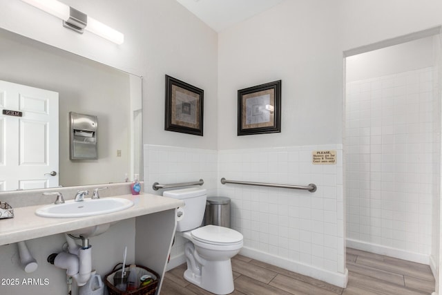 bathroom with tile walls, toilet, wood finished floors, walk in shower, and a sink