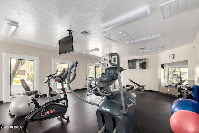 gym featuring plenty of natural light, a textured ceiling, and attic access