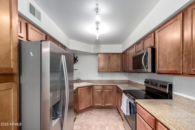 kitchen featuring stainless steel appliances, a sink, brown cabinetry, a textured ceiling, and light countertops