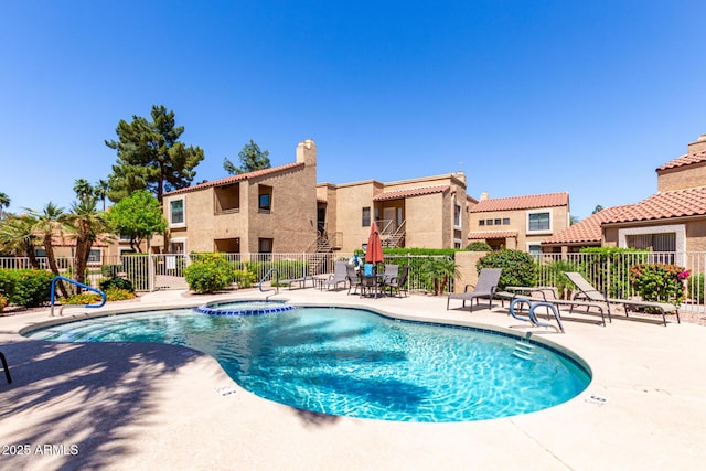 view of swimming pool featuring fence, a pool with connected hot tub, a patio, and a residential view