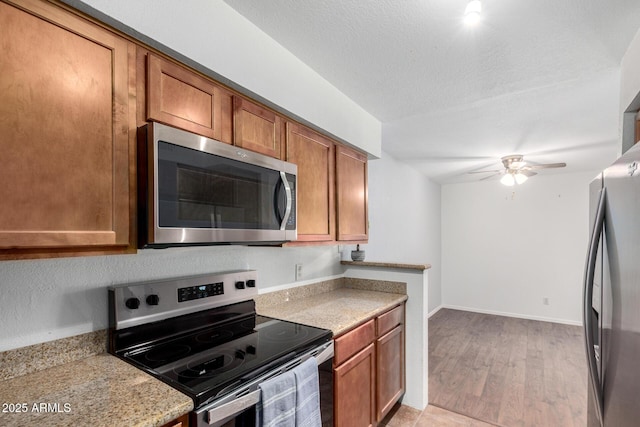 kitchen with stainless steel appliances, ceiling fan, light wood-type flooring, brown cabinetry, and a textured ceiling