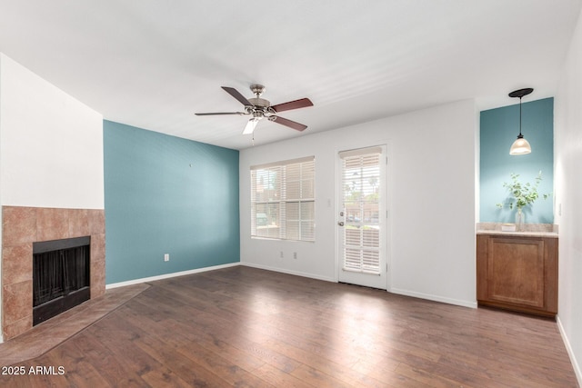 unfurnished living room with a ceiling fan, wood finished floors, a tile fireplace, and baseboards