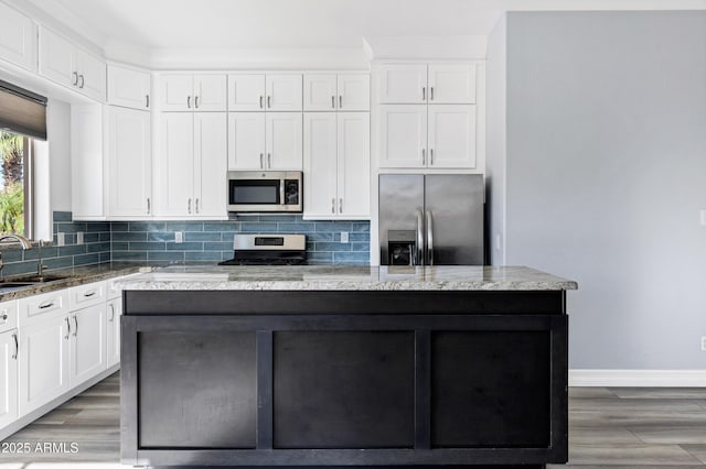 kitchen featuring decorative backsplash, a kitchen island, baseboards, white cabinets, and stainless steel appliances