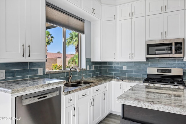 kitchen featuring appliances with stainless steel finishes, tasteful backsplash, a sink, light stone counters, and white cabinetry