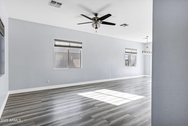 empty room featuring baseboards, ceiling fan, visible vents, and wood finished floors