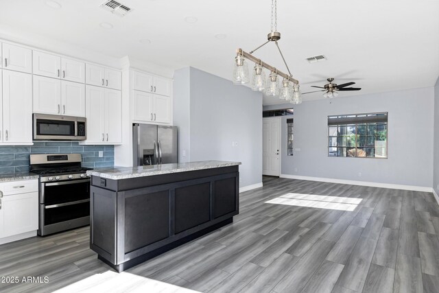 kitchen with a kitchen island, a ceiling fan, appliances with stainless steel finishes, and visible vents
