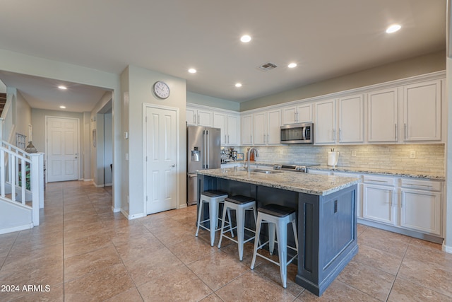 kitchen with appliances with stainless steel finishes, a kitchen island with sink, sink, white cabinetry, and a breakfast bar area