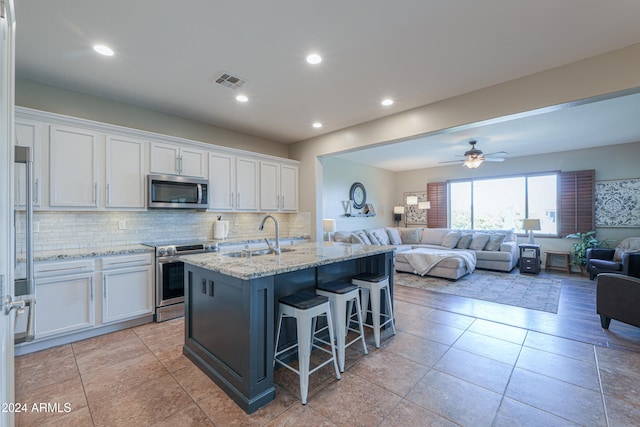 kitchen featuring white cabinets, a kitchen breakfast bar, sink, an island with sink, and stainless steel appliances