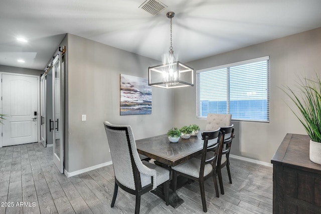 dining space featuring a barn door, an inviting chandelier, and light hardwood / wood-style flooring