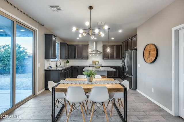 kitchen with wall chimney range hood, sink, hanging light fixtures, decorative backsplash, and appliances with stainless steel finishes