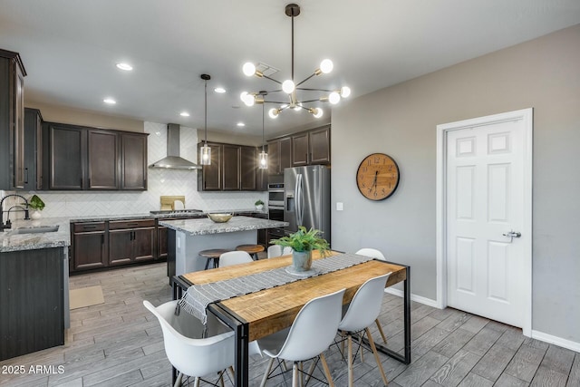 kitchen featuring sink, wall chimney exhaust hood, hanging light fixtures, a kitchen island, and appliances with stainless steel finishes