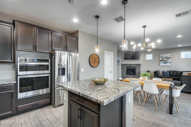 kitchen with a stone fireplace, pendant lighting, stainless steel appliances, and dark brown cabinets