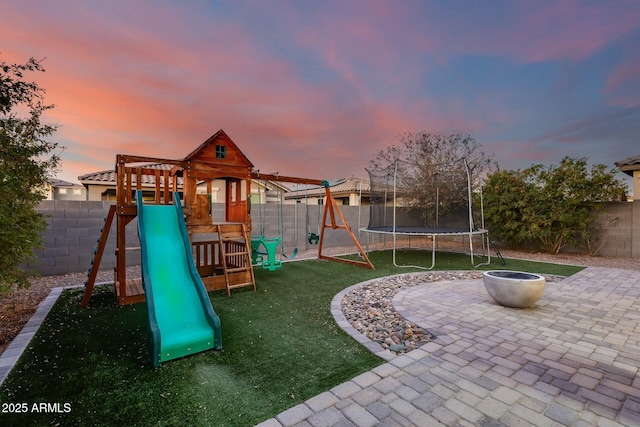 playground at dusk with a lawn, a patio area, and a trampoline