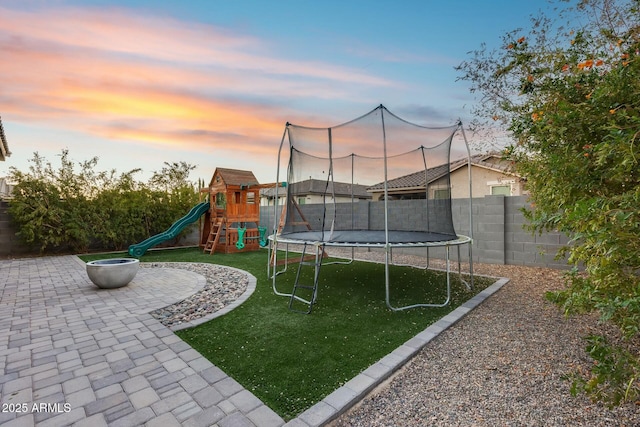 yard at dusk featuring a playground, a trampoline, and a patio