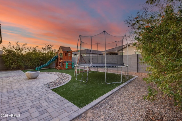 yard at dusk featuring a playground, a patio area, and a trampoline