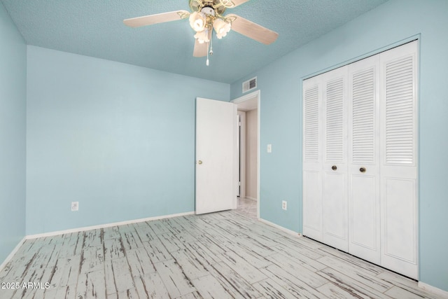 unfurnished bedroom with wood finished floors, visible vents, baseboards, a closet, and a textured ceiling