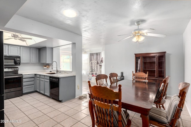 kitchen featuring light countertops, light tile patterned floors, gray cabinets, black appliances, and a sink