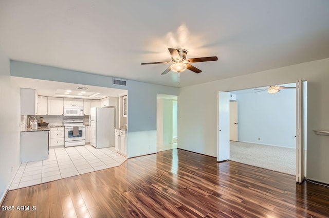 unfurnished living room featuring ceiling fan, sink, and light wood-type flooring