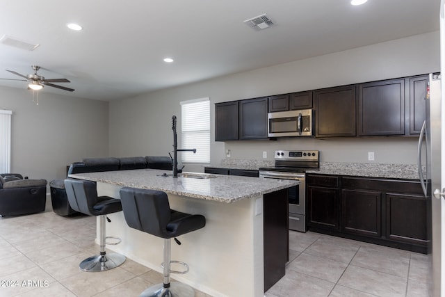 kitchen with sink, a kitchen island with sink, a breakfast bar, light stone countertops, and appliances with stainless steel finishes