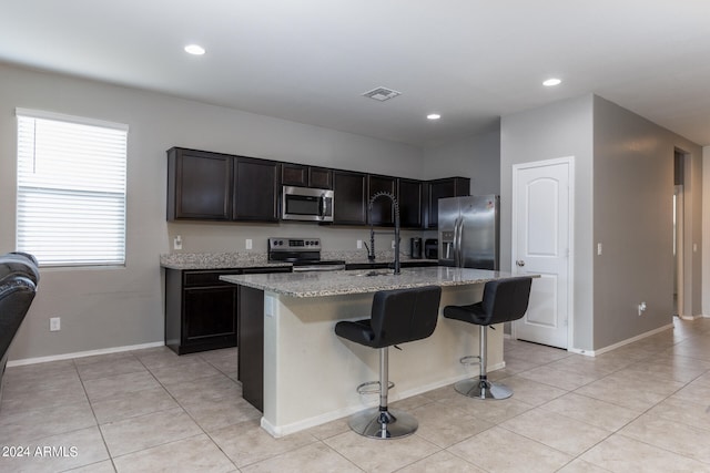 kitchen featuring a kitchen bar, a center island with sink, light stone counters, sink, and appliances with stainless steel finishes