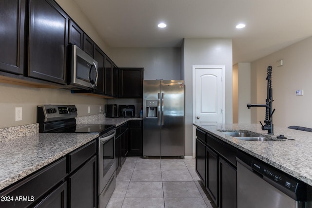 kitchen featuring stainless steel appliances, light tile patterned floors, light stone counters, and sink