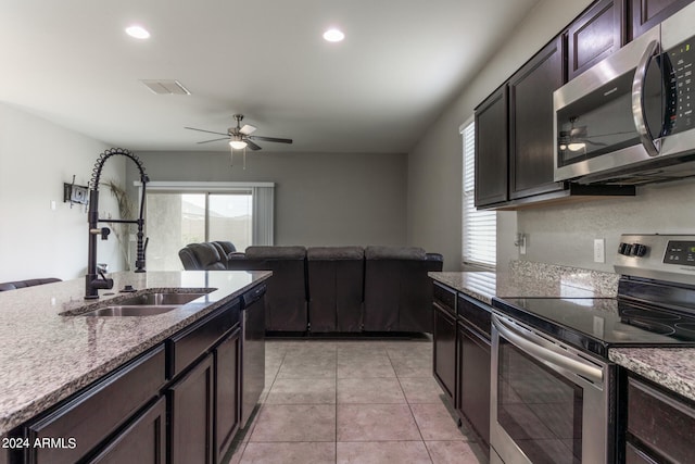 kitchen with stainless steel appliances, light stone counters, sink, light tile patterned flooring, and dark brown cabinets