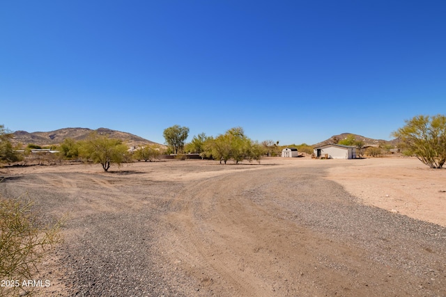 view of yard featuring an attached garage, a mountain view, dirt driveway, and a storage shed