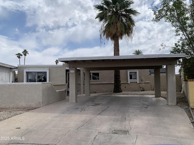 rear view of property with fence, stucco siding, an attached carport, driveway, and brick siding