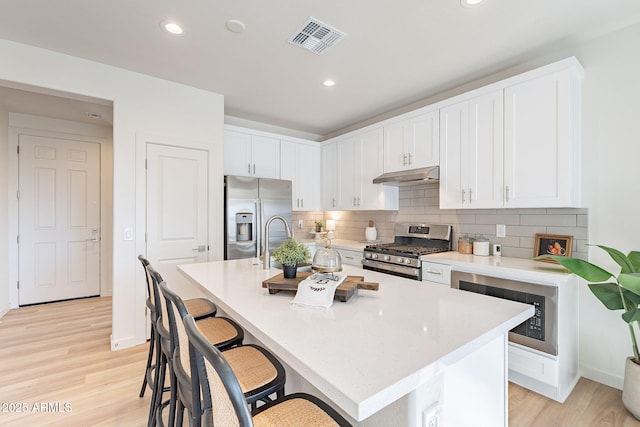 645 N Vine St, Chandler, AZ 85225 - kitchen with appliances with stainless steel finishes, under cabinet range hood, a kitchen breakfast bar, white cabinets, and light countertops