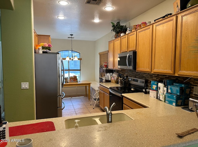 kitchen with a textured ceiling, a notable chandelier, backsplash, hanging light fixtures, and stainless steel appliances