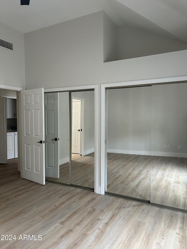 unfurnished bedroom with washing machine and clothes dryer, multiple closets, and high vaulted ceiling