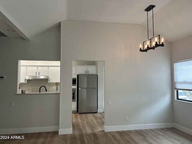 kitchen with pendant lighting, vaulted ceiling, tasteful backsplash, white cabinetry, and stainless steel appliances