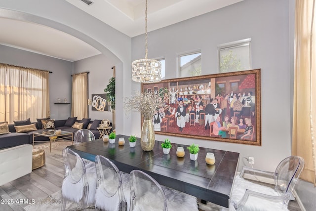 dining space featuring an inviting chandelier, wood finished floors, a healthy amount of sunlight, and arched walkways