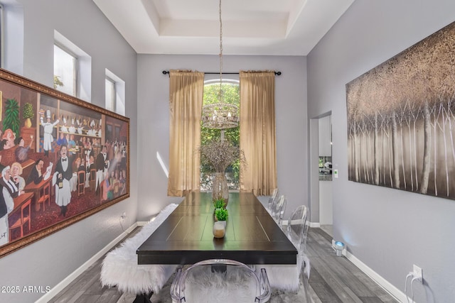 dining area with wood finished floors, a tray ceiling, a chandelier, and baseboards