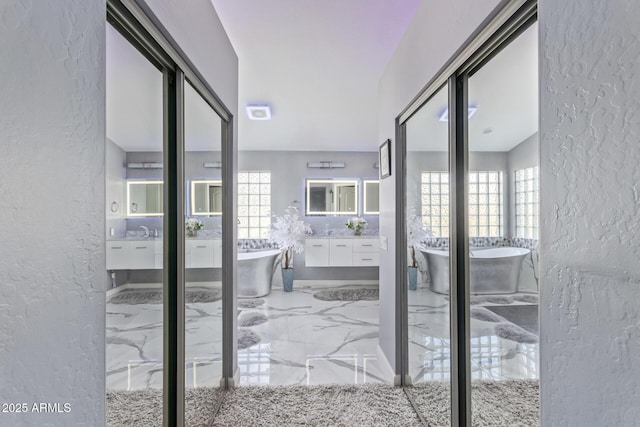 full bathroom with vanity, marble finish floor, a textured wall, and a soaking tub