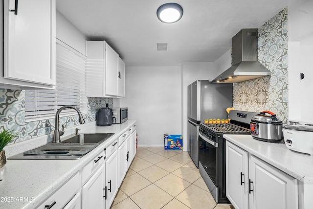 kitchen with light tile patterned flooring, sink, white cabinetry, stainless steel appliances, and wall chimney range hood