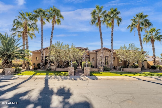 mediterranean / spanish house featuring stone siding, a tiled roof, a front lawn, and stucco siding