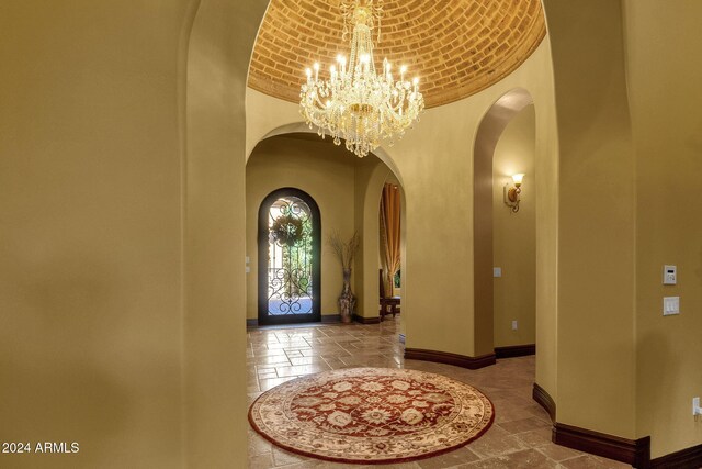 foyer featuring baseboards, arched walkways, brick ceiling, an inviting chandelier, and stone tile flooring