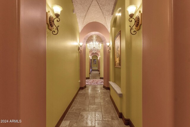 hall with arched walkways, baseboards, lofted ceiling, and stone tile floors