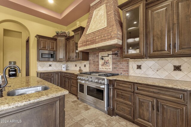 kitchen with stainless steel appliances, custom range hood, a sink, and dark brown cabinets