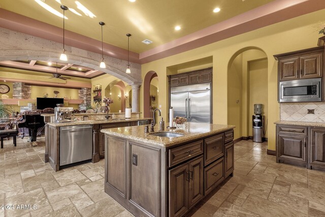 kitchen featuring arched walkways, a sink, stone tile floors, and built in appliances