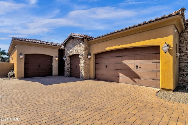 mediterranean / spanish-style house featuring a garage, a tile roof, stone siding, decorative driveway, and stucco siding