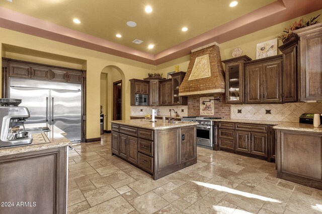 kitchen with built in appliances, premium range hood, arched walkways, and a raised ceiling