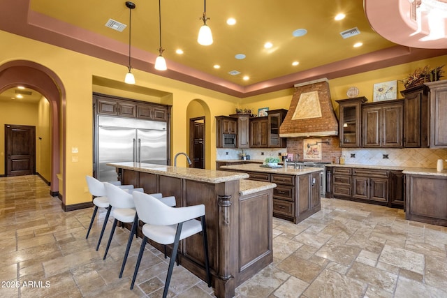 4301 E Taurus Pl, Chandler, AZ 85249 - kitchen featuring a raised ceiling, arched walkways, a center island with sink, appliances with stainless steel finishes, and stone tile flooring