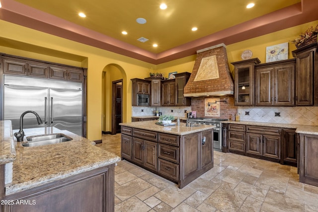 4301 E Taurus Pl, Chandler, AZ 85249 - kitchen with built in appliances, premium range hood, arched walkways, a tray ceiling, and a kitchen island with sink