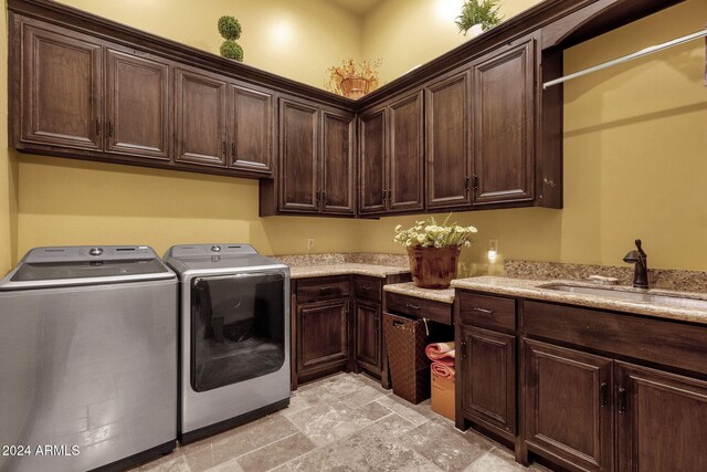 clothes washing area with a sink, stone finish flooring, washing machine and dryer, and cabinet space