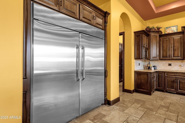 4301 E Taurus Pl, Chandler, AZ 85249 - kitchen with stainless steel built in refrigerator, arched walkways, stone tile floors, tasteful backsplash, and dark brown cabinetry