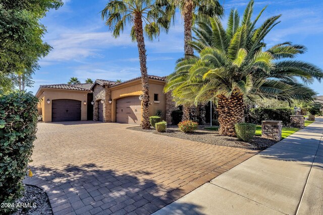 mediterranean / spanish-style house featuring an attached garage, a tiled roof, stone siding, decorative driveway, and stucco siding