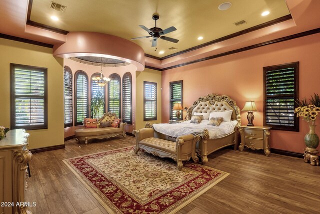 bedroom featuring a tray ceiling, visible vents, ornamental molding, wood finished floors, and a chandelier