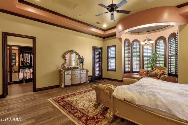 bedroom with a notable chandelier, wood finished floors, baseboards, ornamental molding, and a tray ceiling